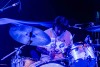 A male presenting musician plays drums on the stage at the Riverside Municipal Auditorium