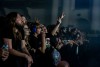 Excited members of a crowd attending a concert scream and put their hands up in support of the band