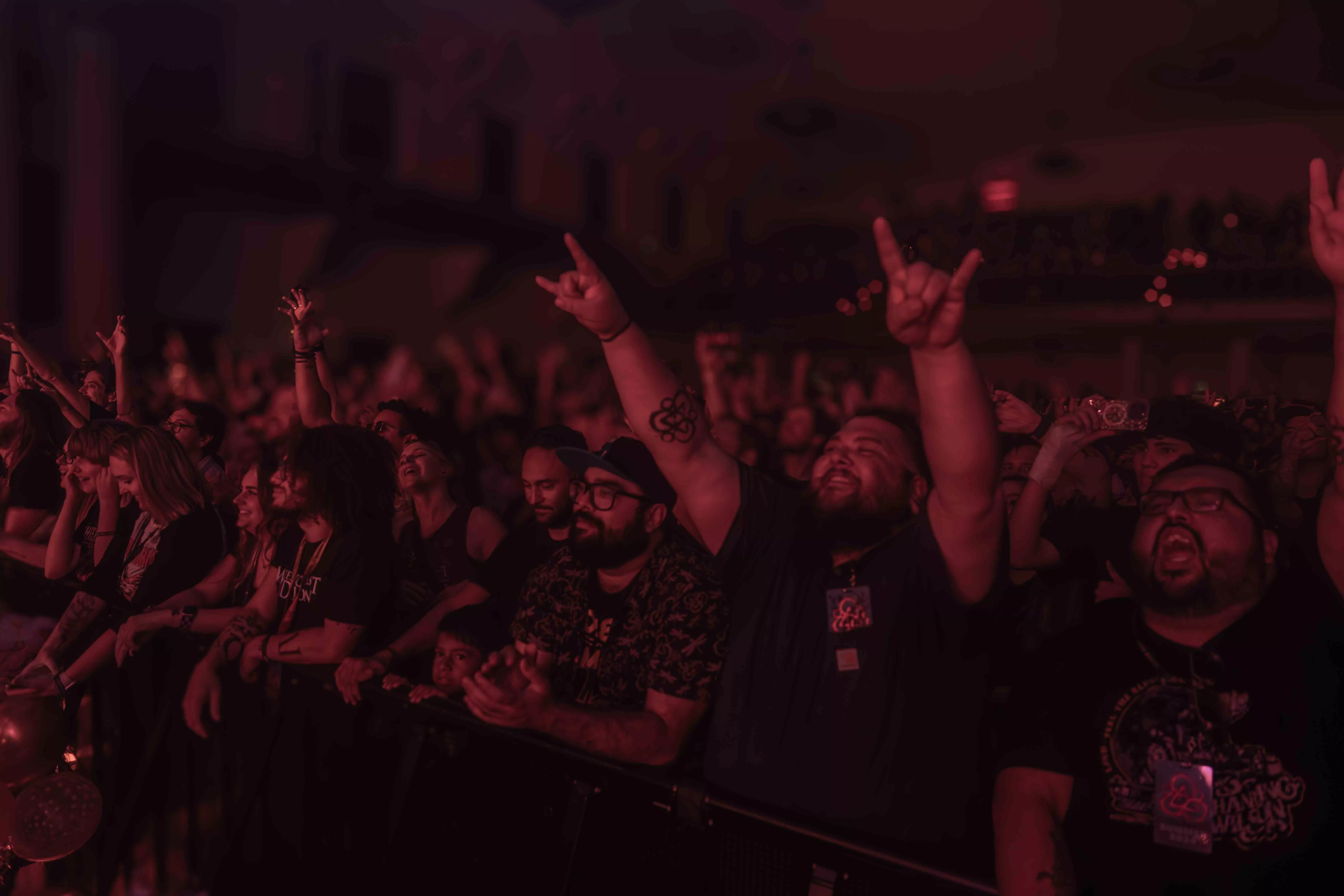 Excited members of a crowd attending a concert scream and put their hands up in support of the band