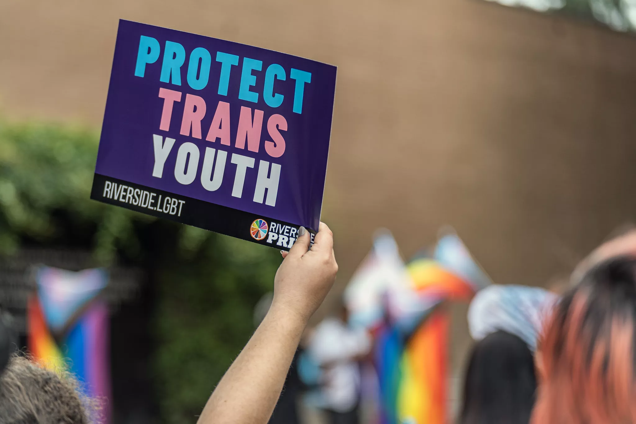 A hand holds up a sign that reads Protect Trans Youth at a rally in support of transgender people