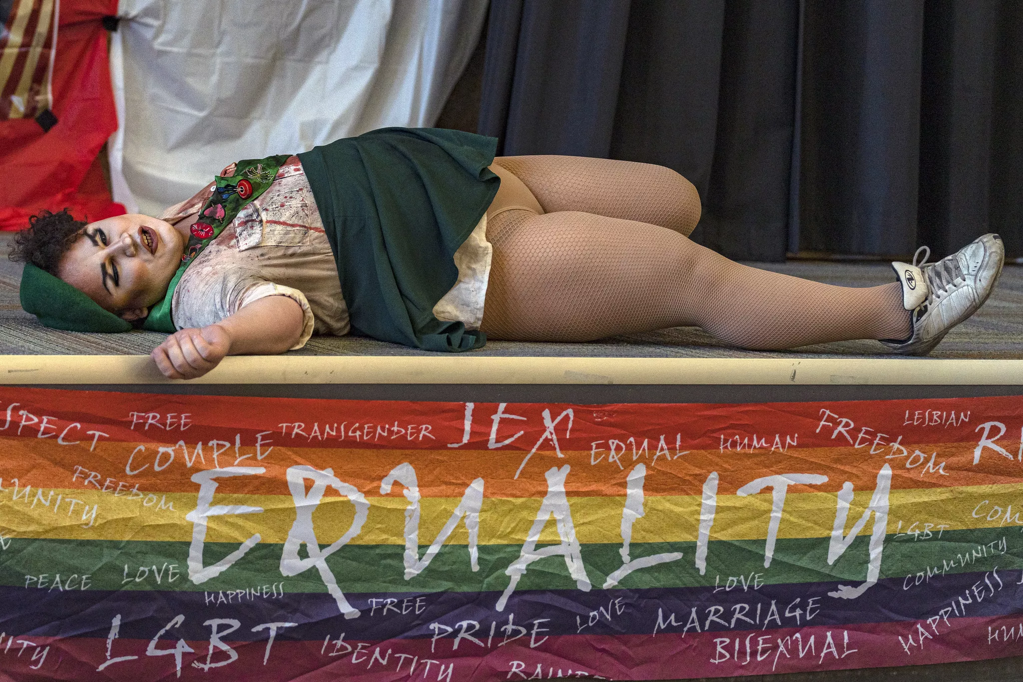 A drag queen lays on the stage with a banner that reads equality and other LGBT buzz words