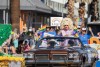 A brown older model car driving a parade route carrying drag queen Trixie Mattel