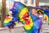 A male presenting person twirls colorful flags with their group