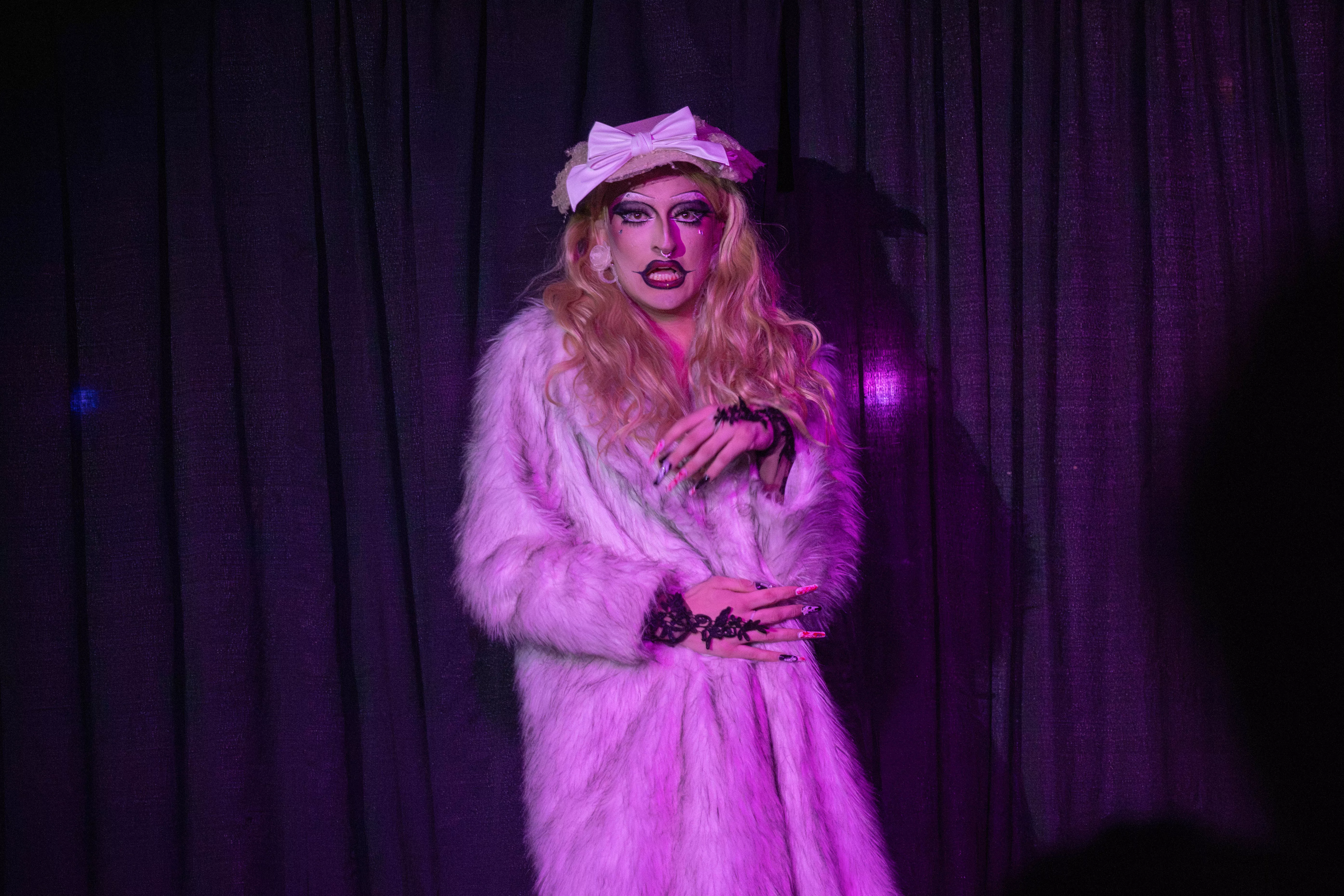 A drag queen in a robe performs on stage