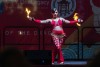 A female presenting person dances with fire wands strapped to their hands