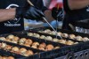 A cook turns Takoyaki balls over with skewers