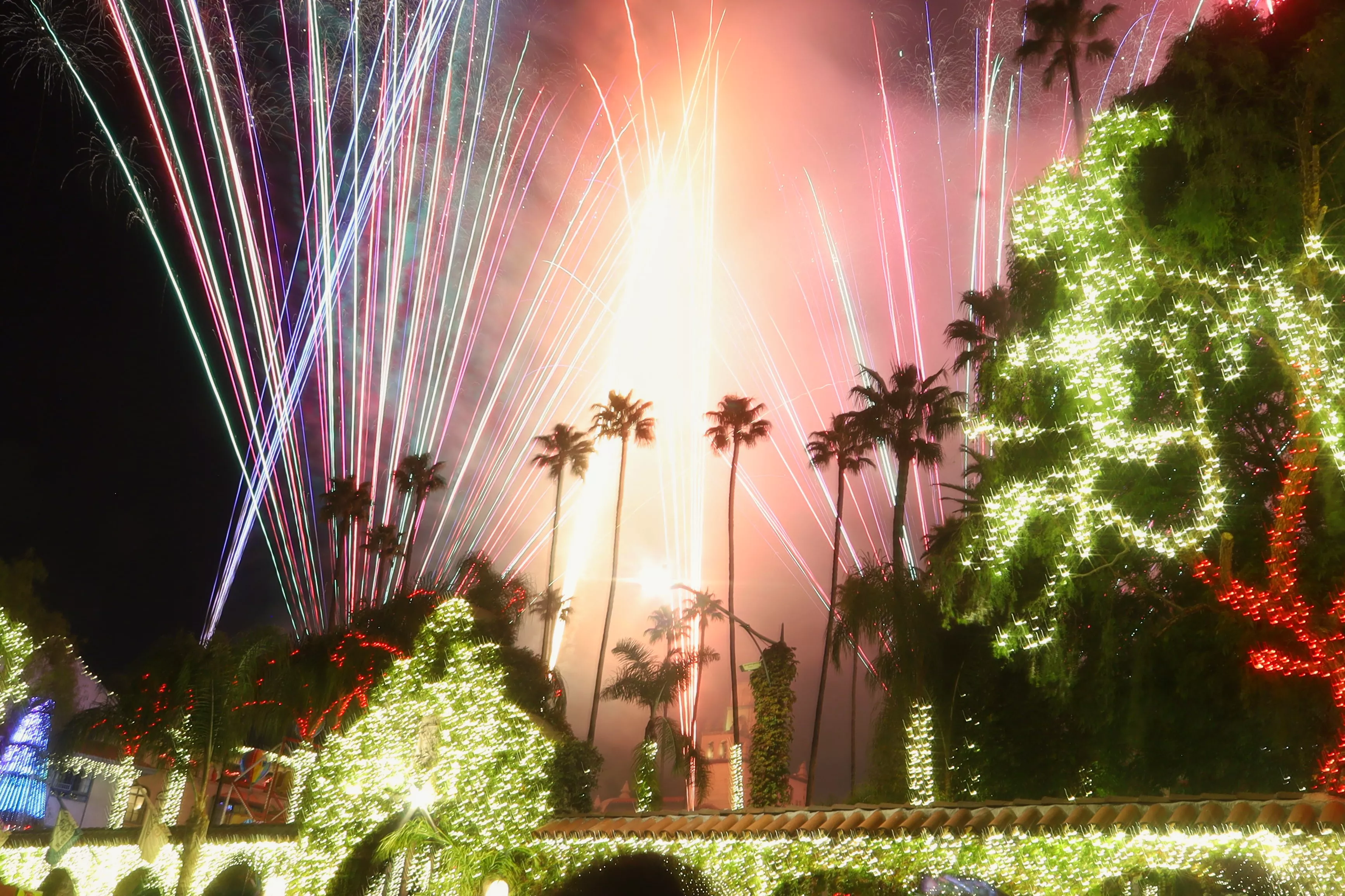 Fireworks stream up over a building completely covered in christmas lights