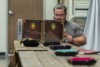 A male presenting person sitting behind a DM screen at a table with dice trays