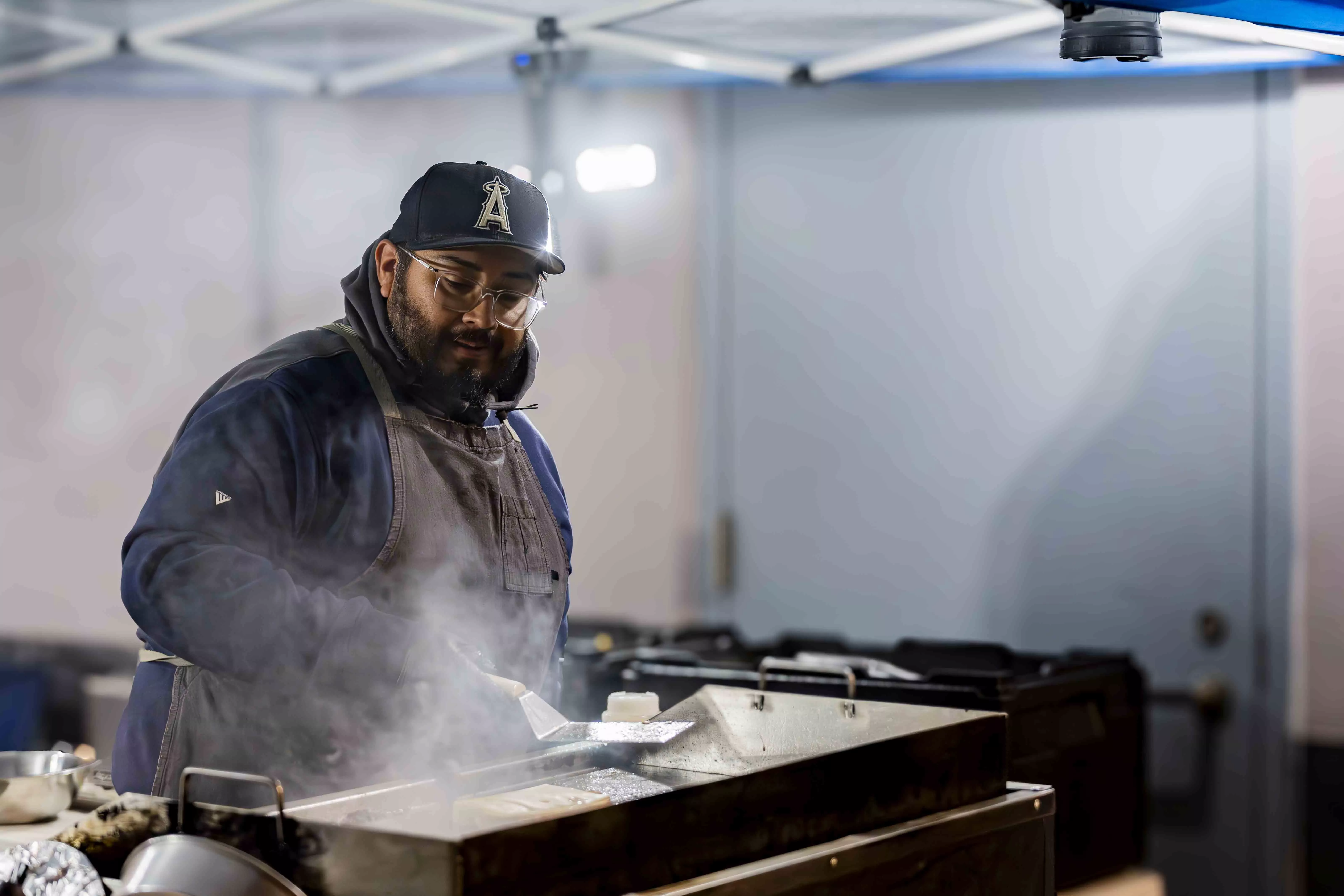 A male presenting person cooking over a steaming grill