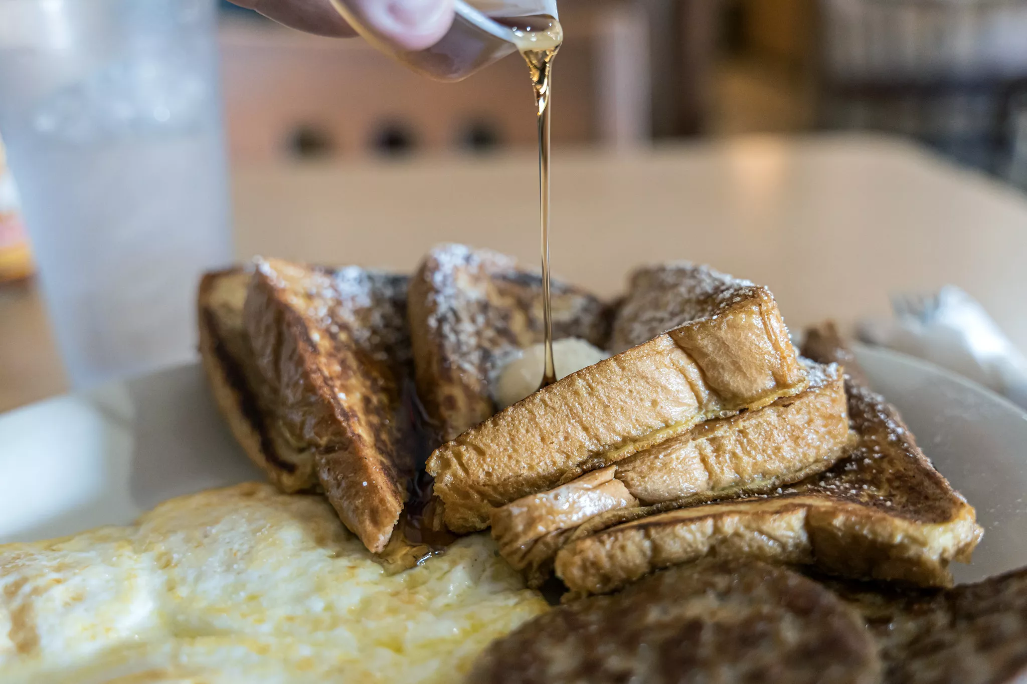 Syrup drizzles over french toast served with eggs and sausage as popular menu item at Joannes Cafe in Riverside on March 22