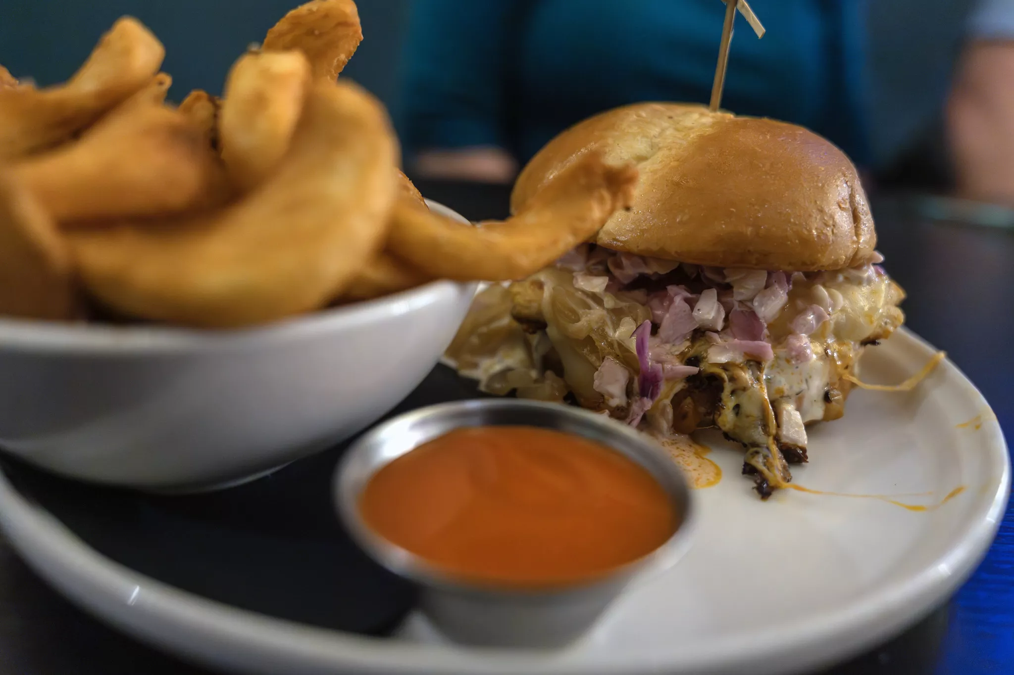 A plate with a spicy chicken sandwich a dipping side of buffalo sauce and a small bowl of fries