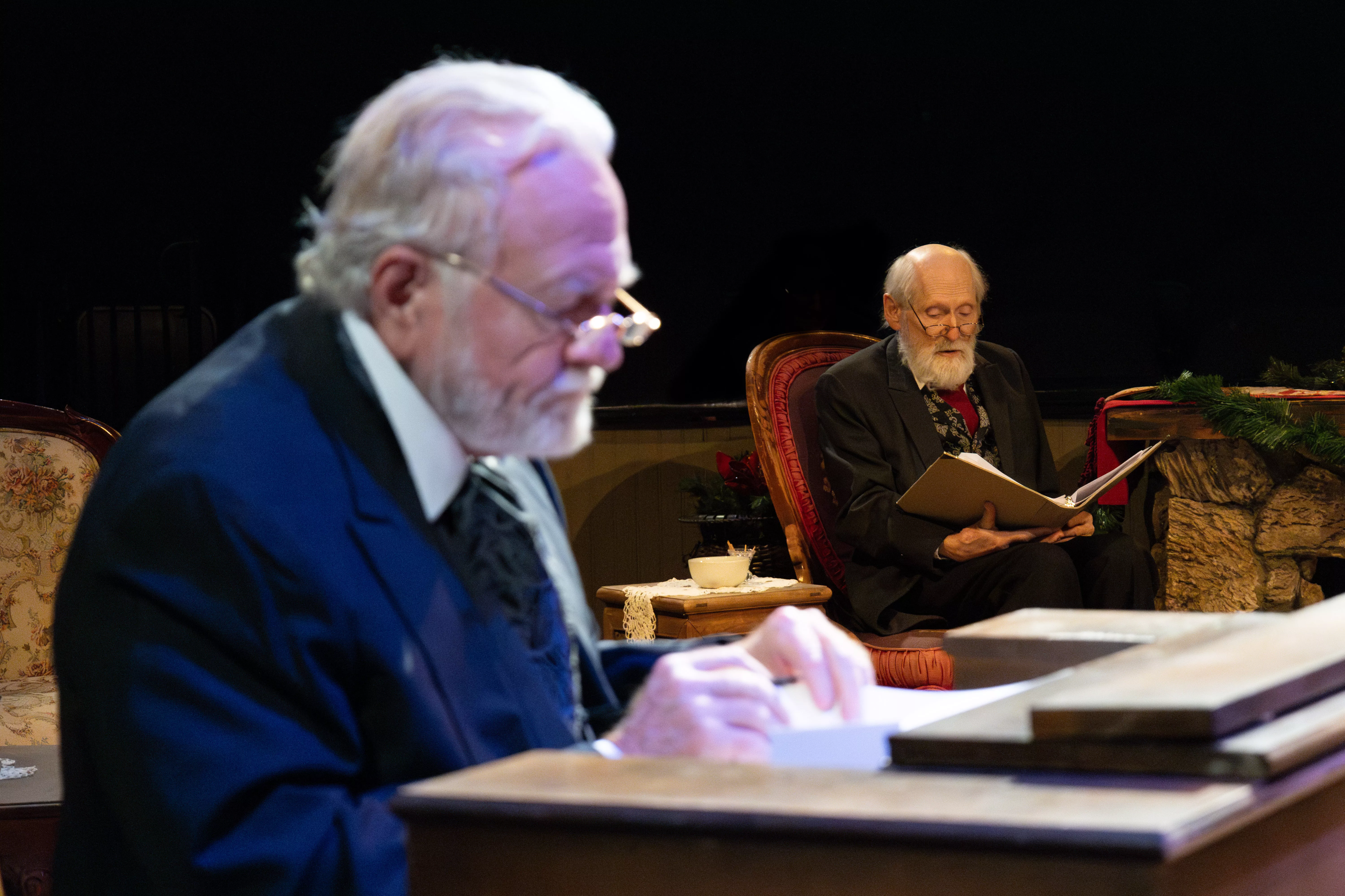 Charles Dickens reads his story in the background as Ebenezer Scrooge works at his desk